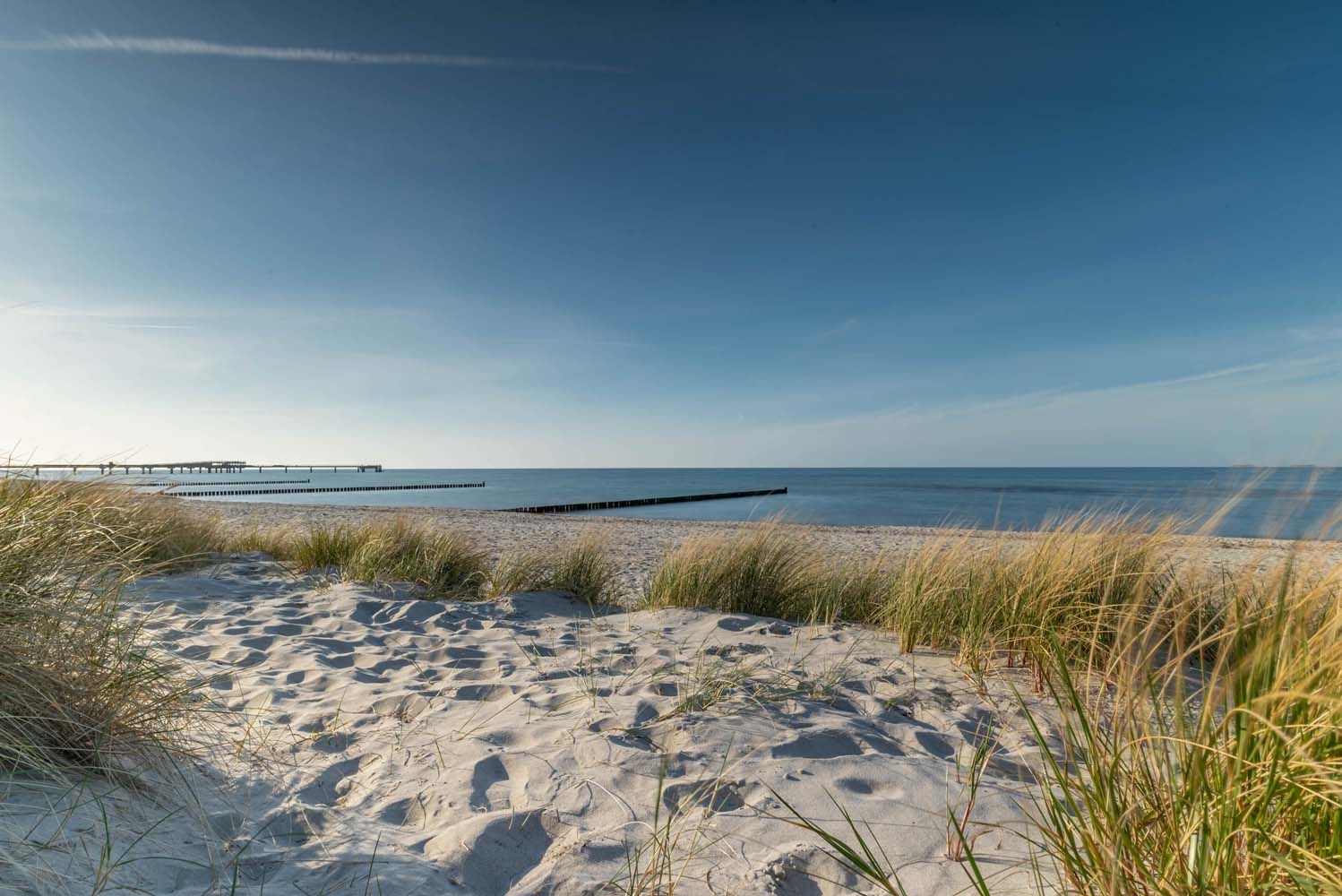Ein Sandstrand mit Wasser und eine Steg