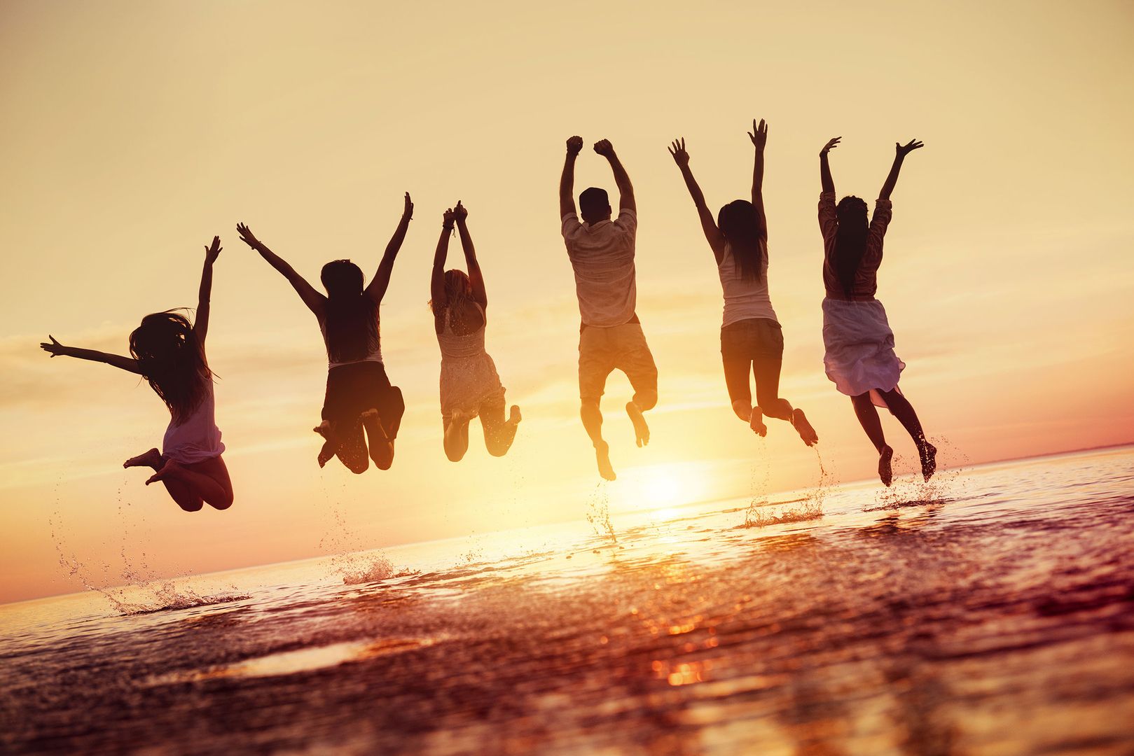 Mehrere Leute springen im Wasser mit einem Sonnenuntergang im Hintergrund